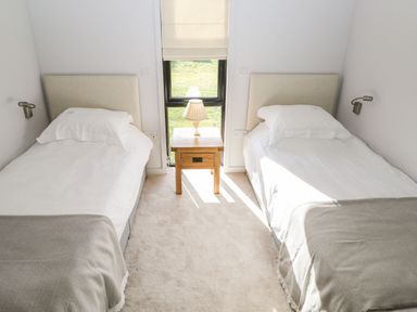 A bedroom with two single beds a wooden nightstand with a lamp and a window at Manor Farm Lodge in Bowerchalke