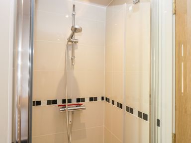 A shower area with a handheld shower head and tiled walls with a black and white tile border at Manor Farm Lodge in Bowerchalke