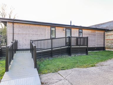 A wooden building with a wheelchair accessible ramp and railing at Manor Farm Lodge in Bowerchalke