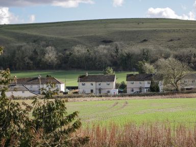 A row of houses with a field and trees in front and a hill in the background at Manor Farm Lodge in Bowerchalke