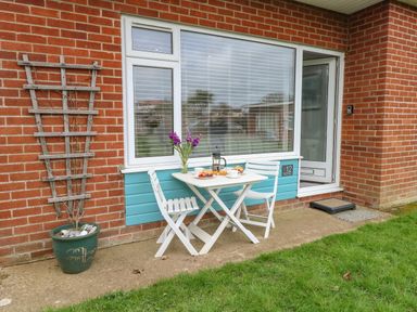A small outdoor patio area with a white table and two chairs set with breakfast at 12 Siesta Mar in Mundesley