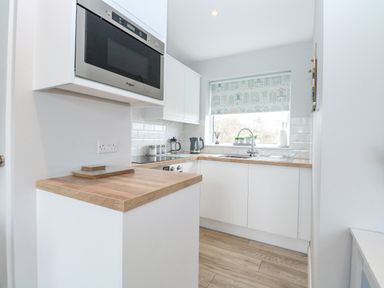 A kitchen with wooden countertops white cabinets a microwave oven and a window with a blind at 12 Siesta Mar in Mundesley