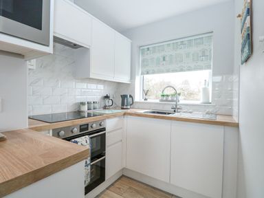 A kitchen with white cabinets wooden countertops a stove sink and a window with a patterned blind at 12 Siesta Mar in Mundesley