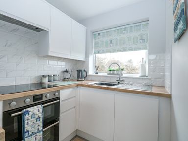 A kitchen with white cabinets wooden countertops an oven a stovetop a sink and a window with a patterned blind at 12 Siesta Mar in Mundesley