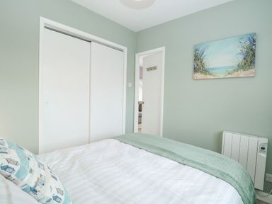 A bedroom with a bed facing a closed white closet door and an open doorway at 12 Siesta Mar Mundesley