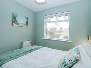 A bedroom with a bed a window with blinds a painting on the wall and a radiator at 12 Siesta Mar in Mundesley