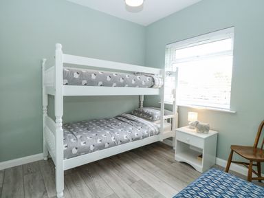 A bedroom with white bunk beds and a nightstand with a lamp and stuffed animal at 12 Siesta Mar in Mundesley