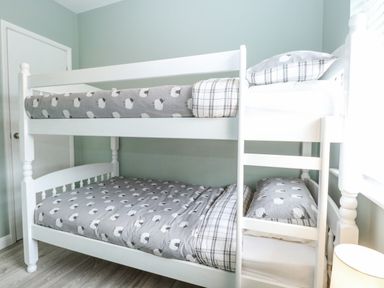 A bedroom with a white bunk bed with grey sheep patterned bedding and a window with blinds at 12 Siesta Mar in Mundesley