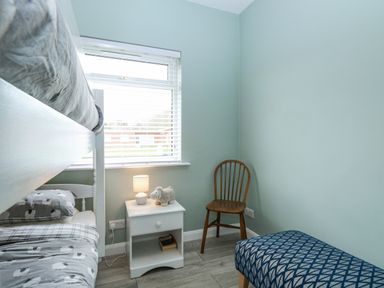 A bedroom with a bunk bed a nightstand with a lamp and toy a wooden chair and a patterned bench at 12 Siesta Mar in Mundesley