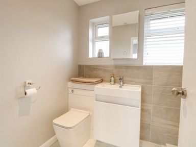 A bathroom with a toilet sink mirror and window blinds at 12 Siesta Mar in Mundesley