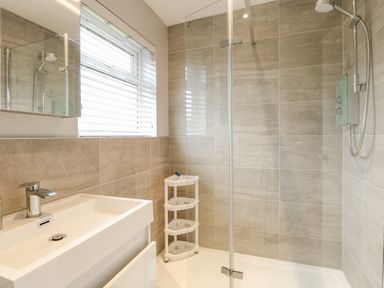 A bathroom with a sink a window with blinds a shower area with glass partition and a white shelf unit at 12 Siesta Mar in Mundesley