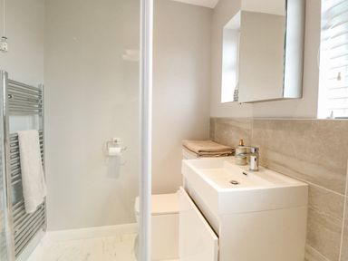 A bathroom with a sink cabinet, mirror cabinet, toilet, towel rail, and window at 12 Siesta Mar in Mundesley