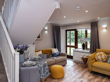 A living room with sofas a knitted footstool dining table under stairs and a door with curtains at The Snug in St Minver