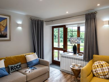 A living room with two sofas one with blue and white cushions and a small wooden table with cups near a window at The Snug in St Minver