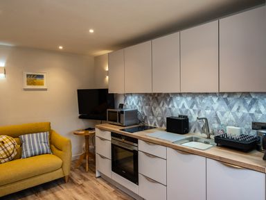 A kitchen with white cabinets wooden countertop and yellow sofa with cushions at The Snug in St Minver