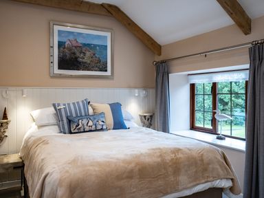 A bedroom with a bed with pillows and a window with curtains and a bird decoration at The Snug in St Minver
