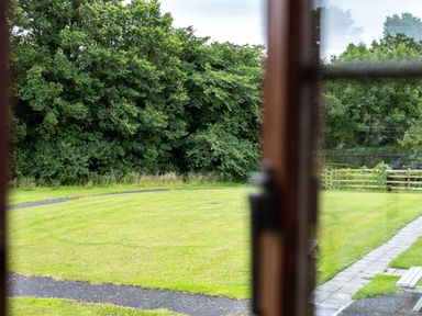 A garden with green grass and a path viewed through a window at The Snug in St Minver