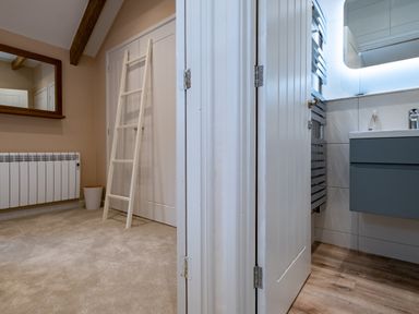 A room with a mirror radiator and ladder next to a bathroom with a sink and wooden floor at The Snug in St Minver