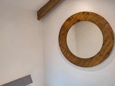 A wall with a round wooden framed mirror and a wooden beam at The Snug in St Minver