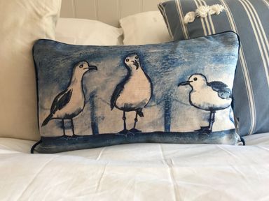 A decorative pillow with a print of three seagulls on a bed with white and striped cushions at The Snug in St Minver