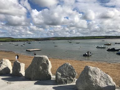 A beach with large rocks in the foreground and boats on the water at The Snug in St Minver