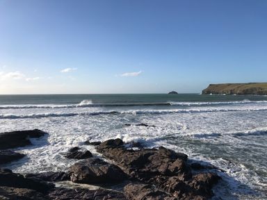 A rocky coastline with waves crashing against the shore and a cliff in the distance at The Snug in St Minver