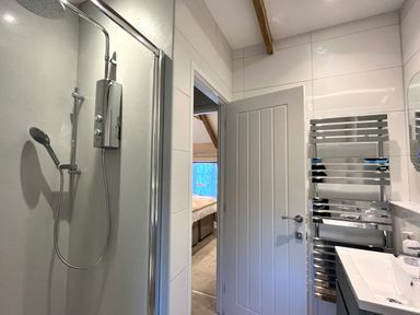 A bathroom with a shower enclosure a towel radiator a sink and an open door showing a bedroom at The Snug in St Minver