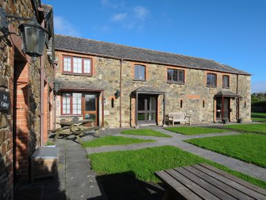 An outdoor area with stone cottages wooden benches and tables on grass at The Snug in St Minver
