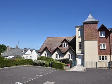 A parking lot with numbered spaces in front of a multi-section building with pitched roofs and multiple windows at 1 Buckfields in Lyme Regis