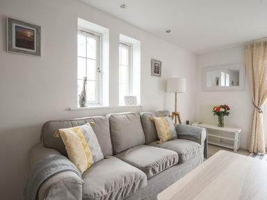 A living room with a grey sofa yellow and grey patterned pillows a floor lamp a large mirror and flowers on a table at 1 Buckfields in Lyme Regis