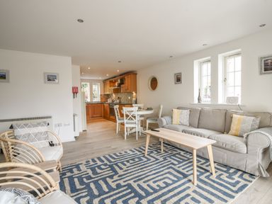 An open living room and kitchen with sofa, armchairs, dining table, and wooden cabinets at 1 Buckfields in Lyme Regis