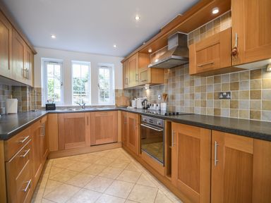 A kitchen with wooden cabinets, tiled floor, and three windows over the sink at 1 Buckfields in Lyme Regis