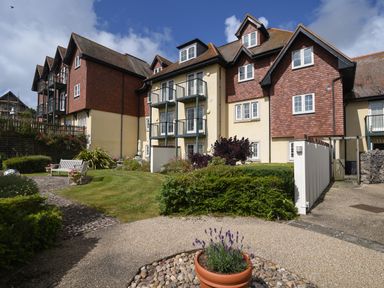 An apartment building with multiple balconies and a landscaped garden with benches and flower pots at 1 Buckfields in Lyme Regis