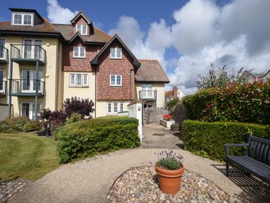 A residential building with balconies surrounded by garden paths bushes and a bench at 1 Buckfields in Lyme Regis