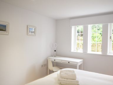 A bedroom with a white desk and chair near a window and folded towels on a bed at 1 Buckfields in Lyme Regis
