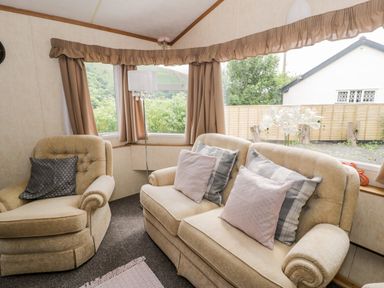 A sitting room with beige armchairs and sofa with cushions and curtains on windows at Grange Caravan in Llangollen