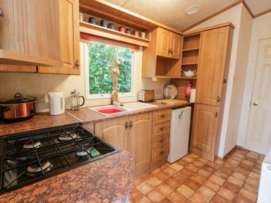 A kitchen with wooden cabinets a stove a sink and a window at Grange Caravan in Llangollen