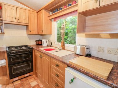 A kitchen with wooden cabinets a black stove a white sink a toaster and a cutting board at Grange Caravan in Llangollen