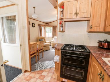 A kitchen with a stove and countertop facing a dining area with chairs and a living room with armchairs at Grange Caravan in Llangollen