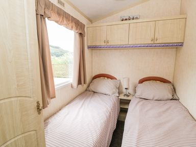 A bedroom with two single beds a window and overhead cabinets at Grange Caravan in Llangollen