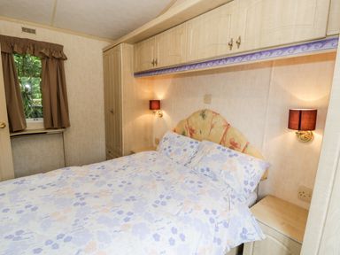 A bedroom with a bed with floral bedding built in cabinets and two bedside lamps at Grange Caravan in Llangollen