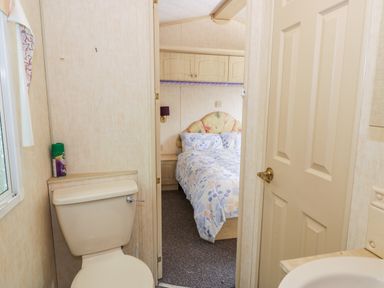 A small bathroom with a toilet and a sink looking into a bedroom with a bed covered in floral bedding at Grange Caravan in Llangollen