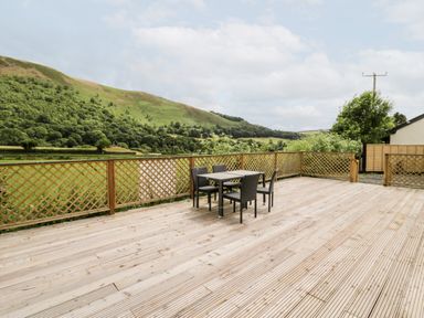 An outdoor wooden deck with a table and four chairs overlooking green hills at Grange Caravan in Llangollen