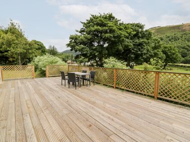 A wooden deck with a table and four chairs overlooking green trees and hills at Grange Caravan in Llangollen
