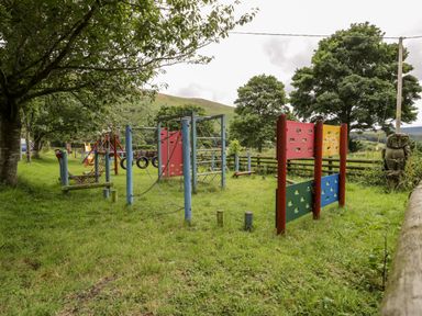 An outdoor playground with climbing structures and swings surrounded by trees and grass at Grange Caravan in Llangollen
