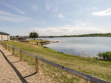 A lakeside with grass an outdoor building and a wooden fence at Lake View Lodge in Wykeham near East Ayton