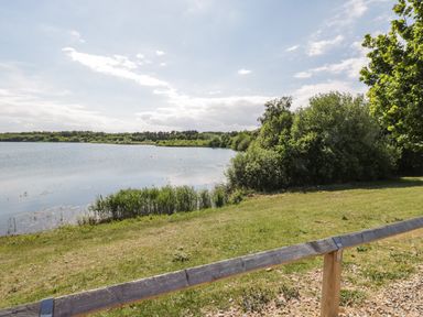 A lake with grass and bushes along the shore and a wooden fence in the foreground at Lake View Lodge in Wykeham near East Ayton