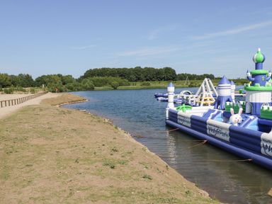 An outdoor lake with inflatable water park structures and a dirt path along the shore at Lake View Lodge in Wykeham near East Ayton