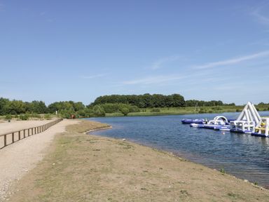 A lake with inflatable water structures and a dirt path with wooden railings at Lake View Lodge in Wykeham near East Ayton
