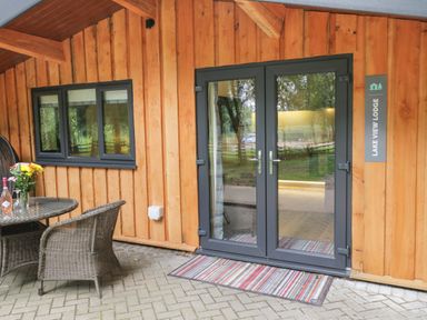 Wooden exterior with glass double doors and a window next to a round table and two wicker chairs at Lake View Lodge Wykeham near East Ayton